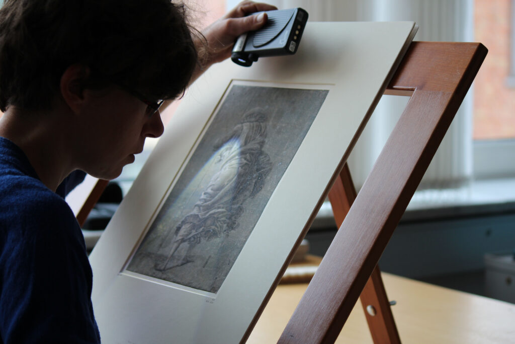 Restauratorin Luise Maul betrachtet eine Zeichnung im Streiflicht (Foto: Staatliche Museen zu Berlin, Kupferstichkabinett, Christof Hannemann)